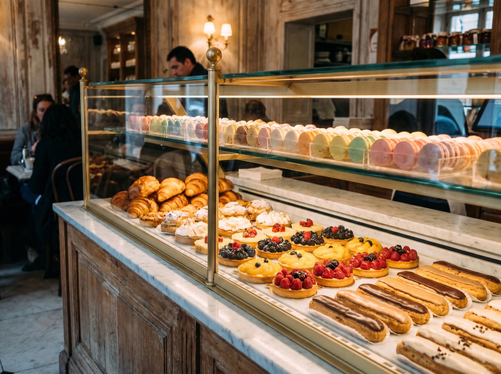 A pâtisserie display case filled with rows of macarons, croissants and tarts